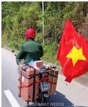 Cựu chiến binh Nguyễn Văn Thanh đi xe máy chở hành lý và cờ đỏ sao vàng